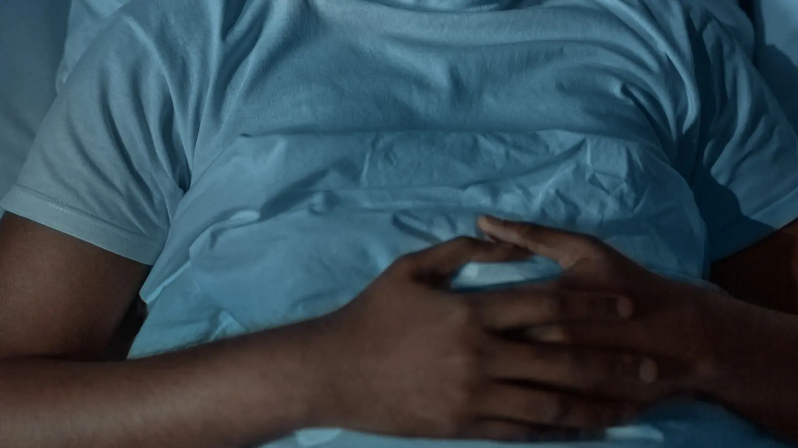 A person lying awake in a dark bedroom, eyes open, with faint light coming through the window