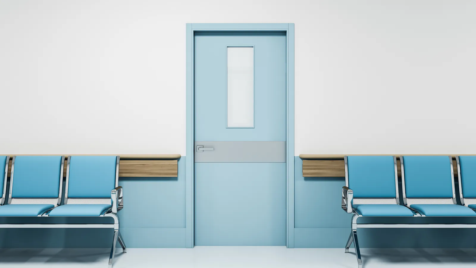 A row of blue chairs beside a closed door in an empty hospital corridor