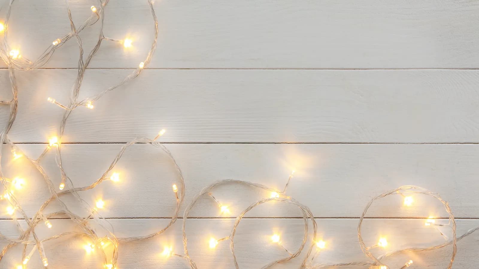A string of small holiday lights lying on white wooden boards