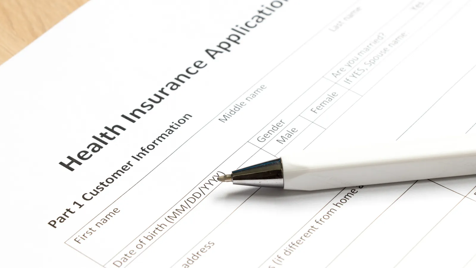 A health insurance application form on a desk with a pen resting on it