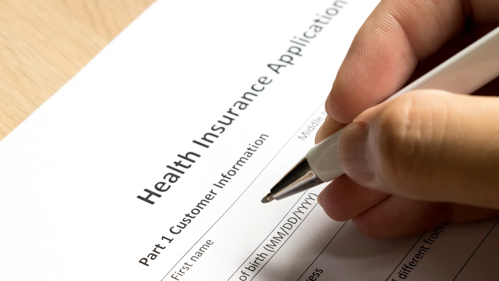 A hand holding a pen over a health insurance application form on a desk