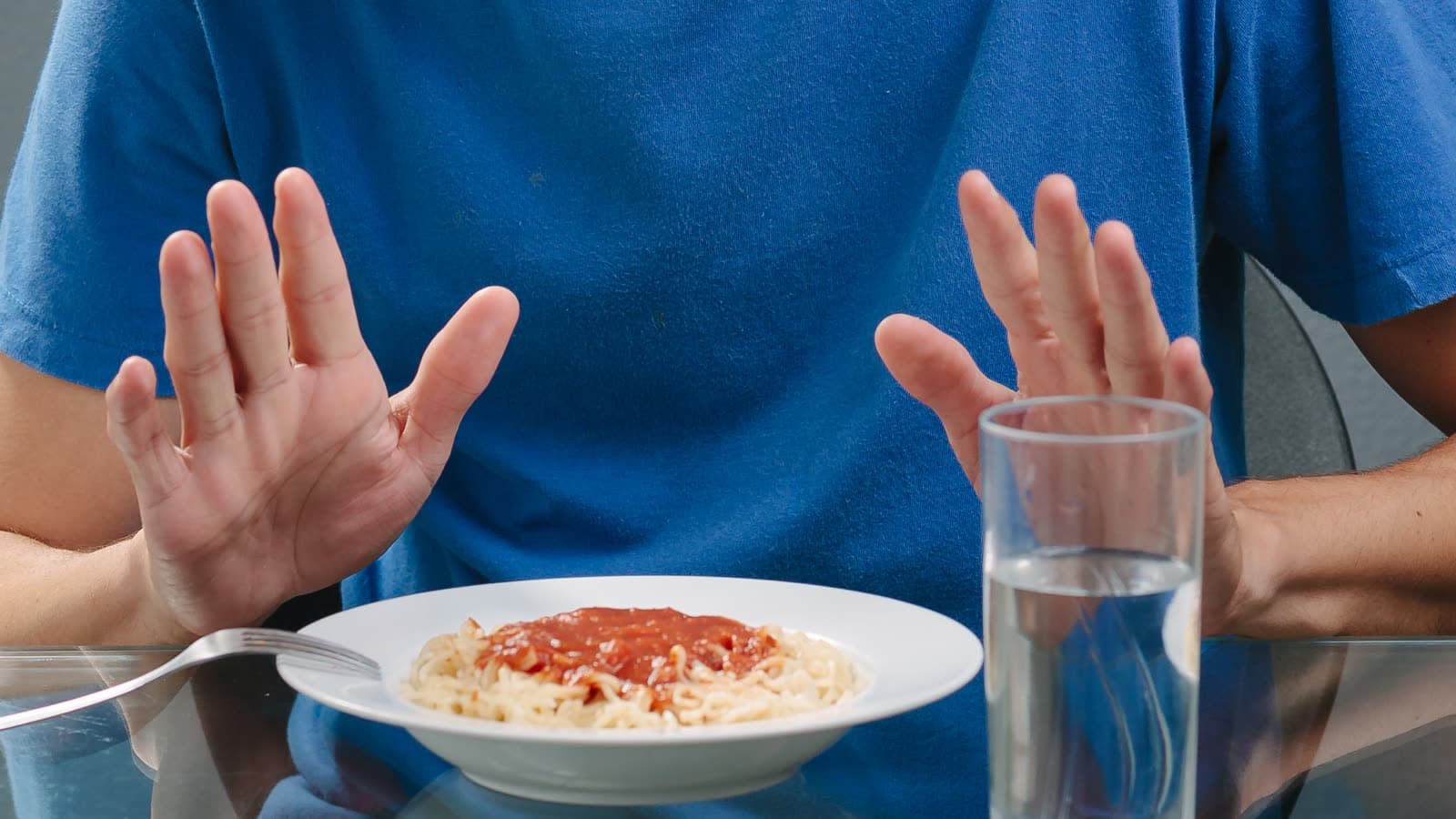A person holds both hands above a plate of pasta.