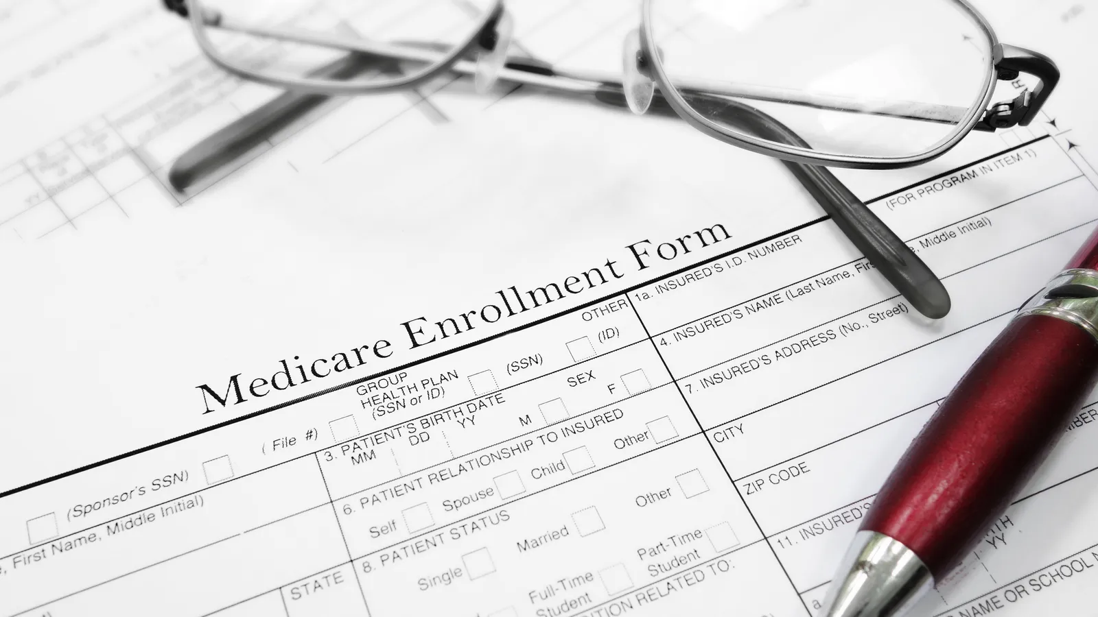 A Medicare enrollment form on a desk with reading glasses and a pen