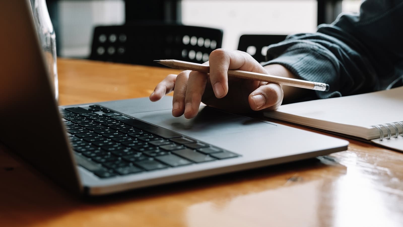 A hand holds a pencil above a laptop keyboard.
