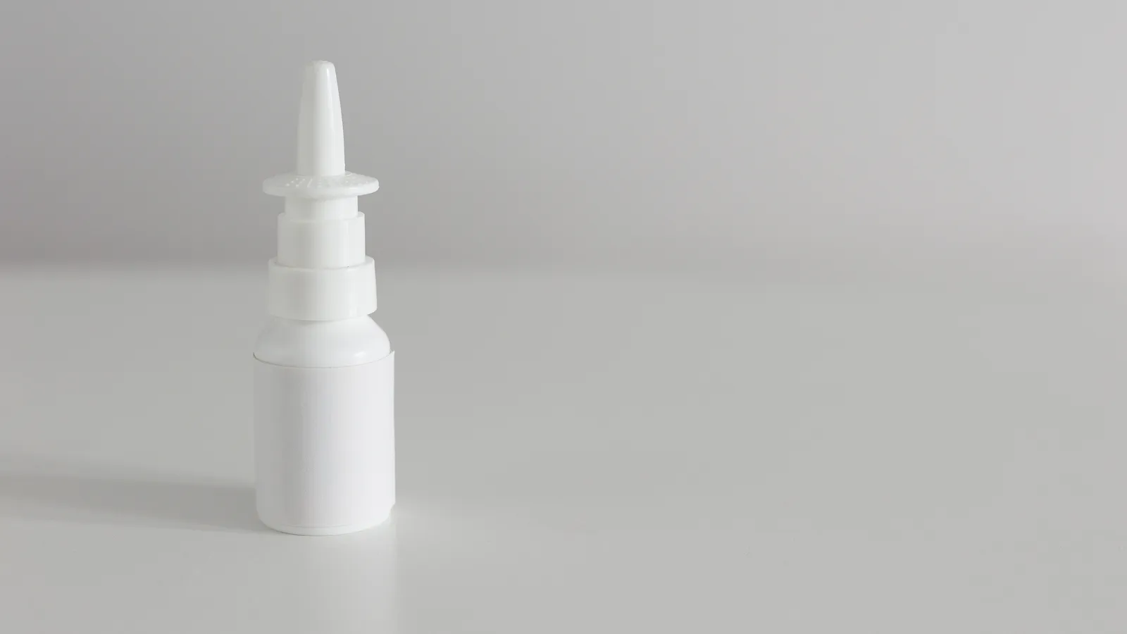A white nasal spray bottle without a label standing on a wooden table