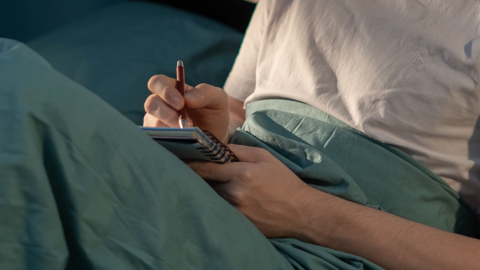 Una persona escribe en un cuaderno mientras está sentada en la cama.