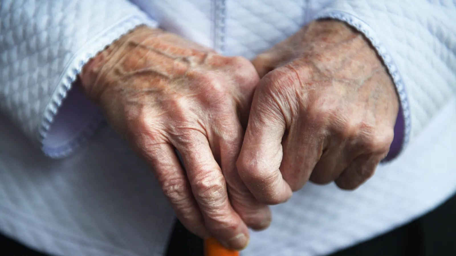 An older person's hands resting on the handle of a cane