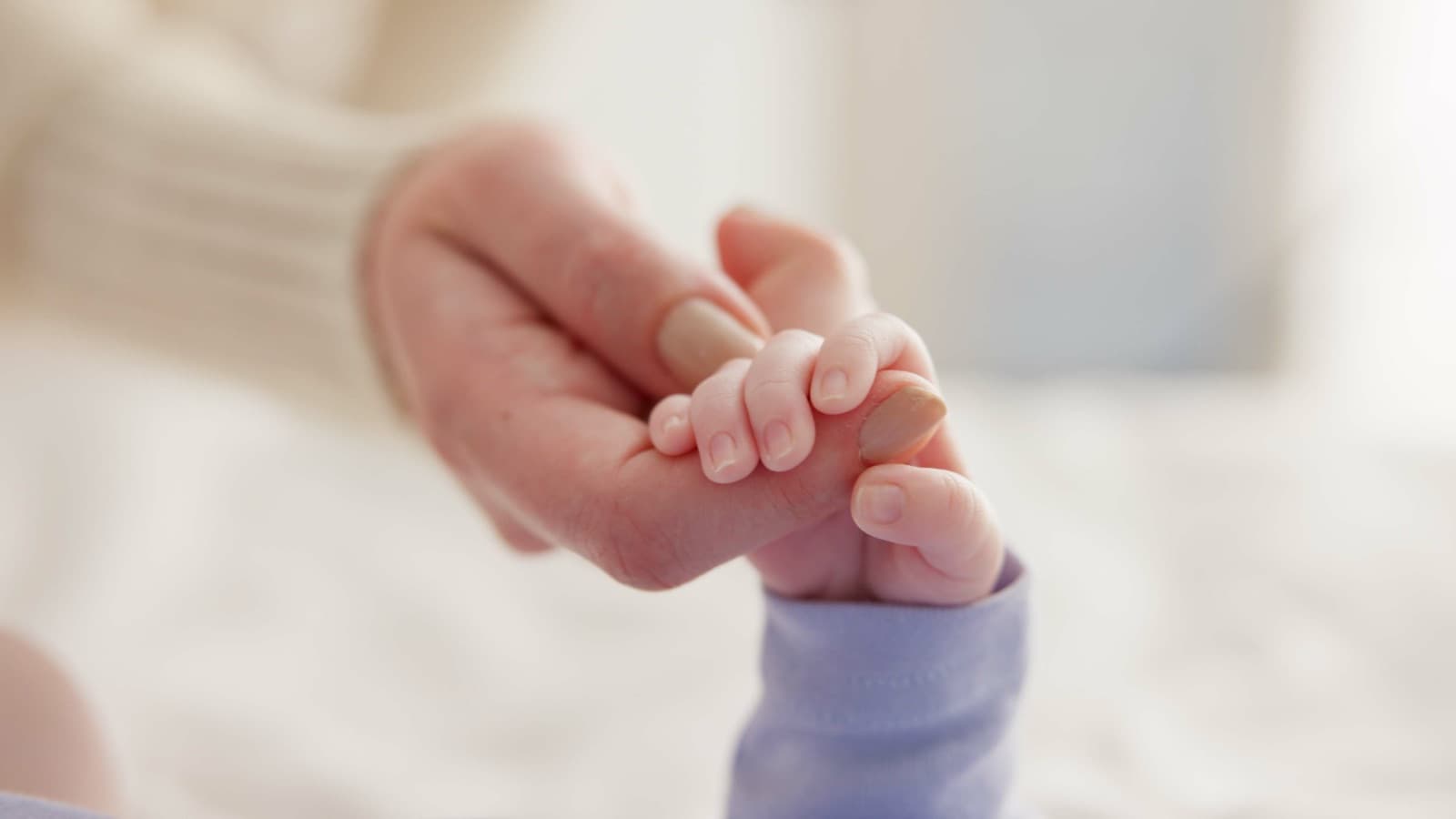 A newborn's hand holds an adult's finger.