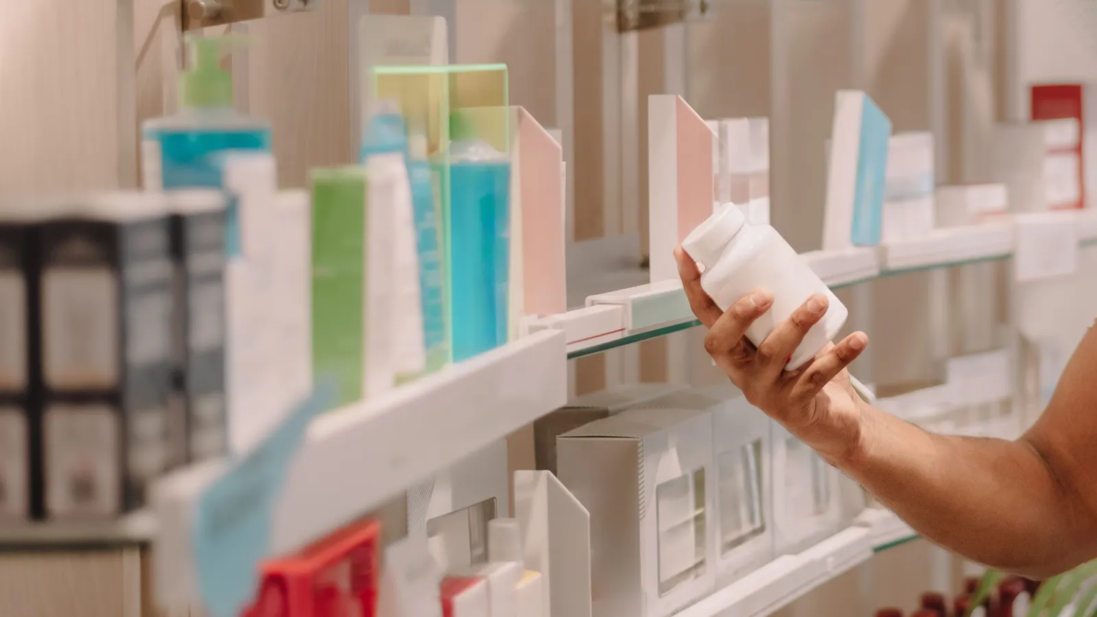 A hand taking a white medicine bottle from a pharmacy shelf