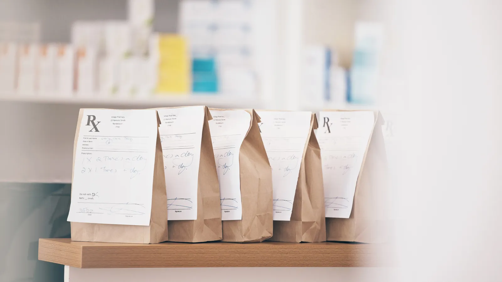 Paper pharmacy bags with prescription labels lined up on a wooden shelf