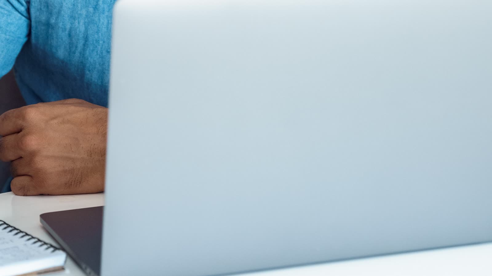 A person's hand rests beside an open laptop and notebook.