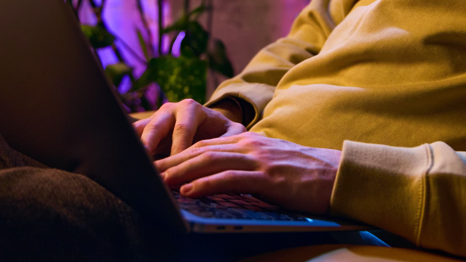 Unas manos escriben en una computadora portátil bajo una luz interior cálida.