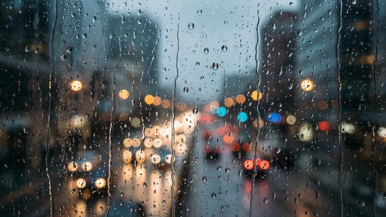 Rain running down a window at night with blurred city lights and traffic beyond