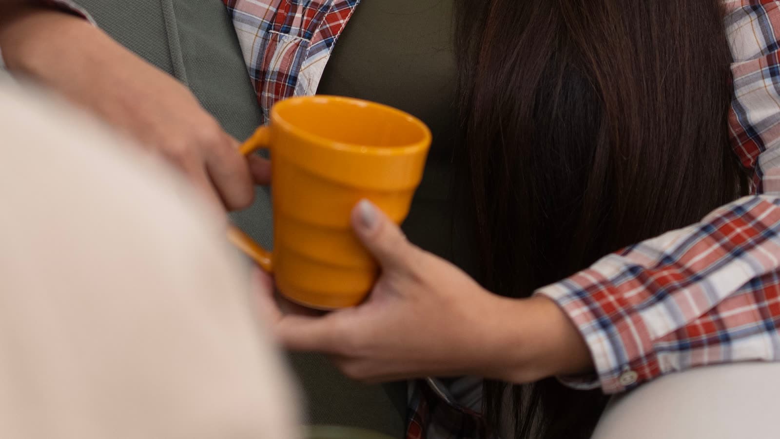Una persona sostiene una taza naranja junto a una segunda persona desenfocada.