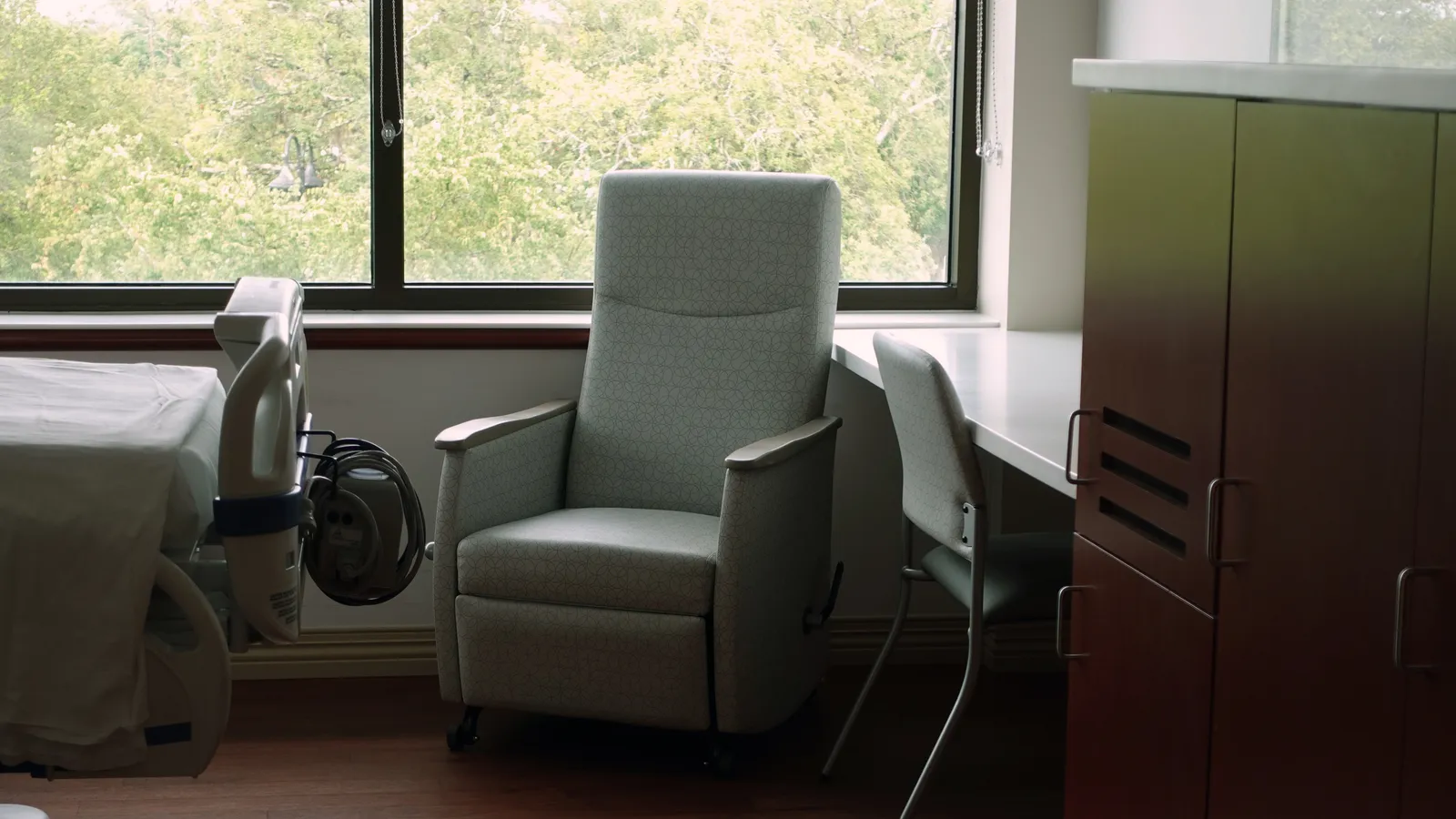 An empty recliner chair beside a window and a desk in a clinic room