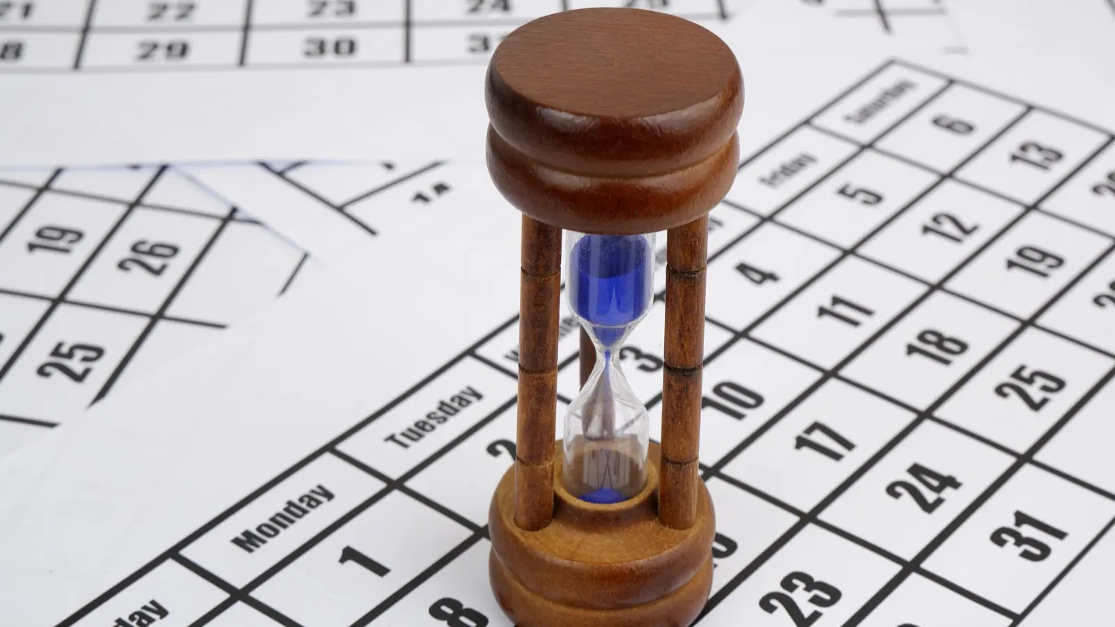 A desk calendar with several dates circled, next to a clock and a pen