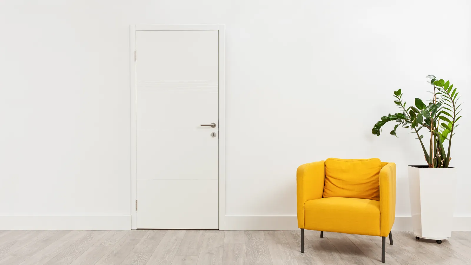 A yellow armchair and a potted plant beside a closed door in a bright waiting room
