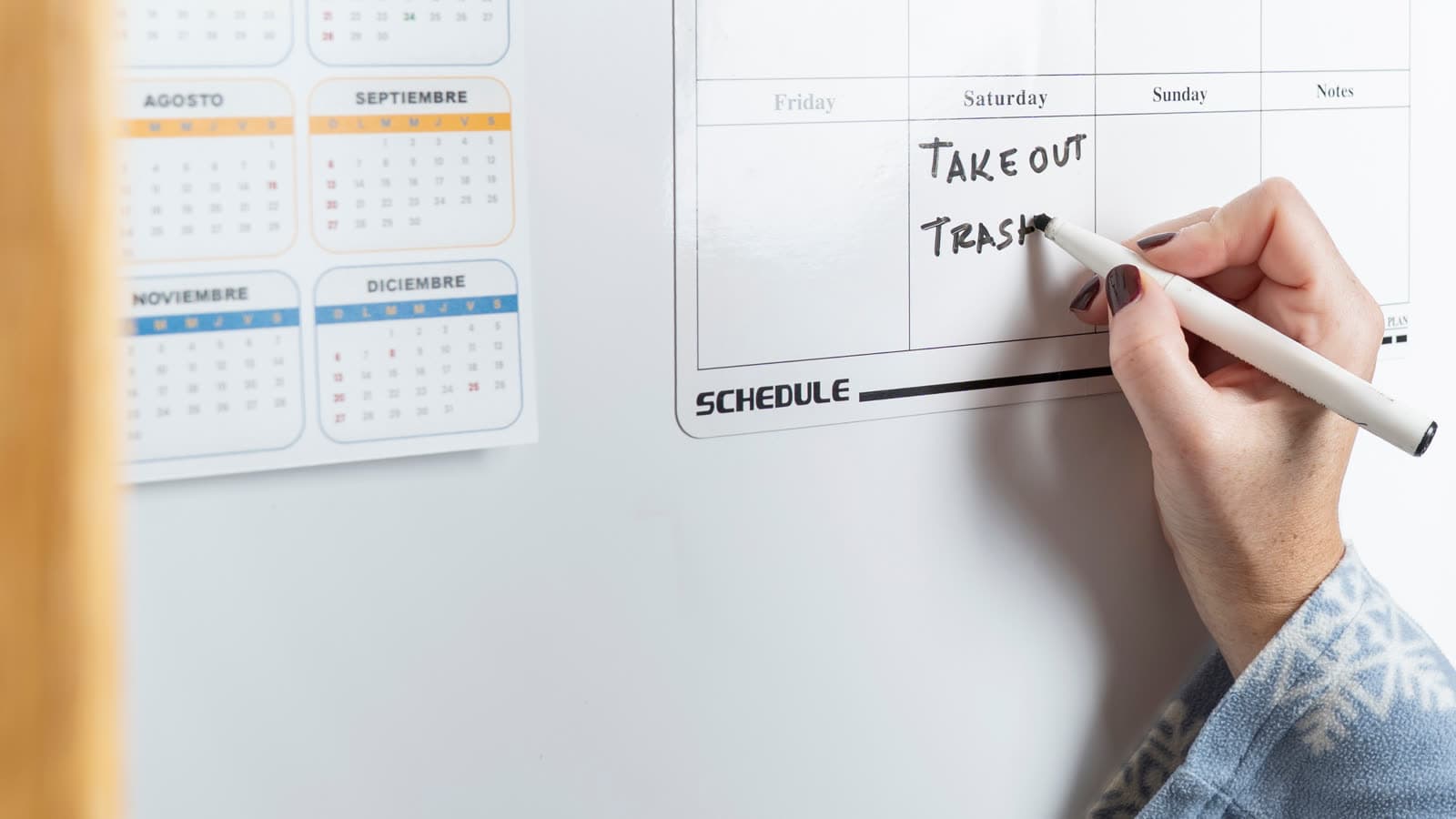 A hand writes on a weekly planner beside calendar pages.