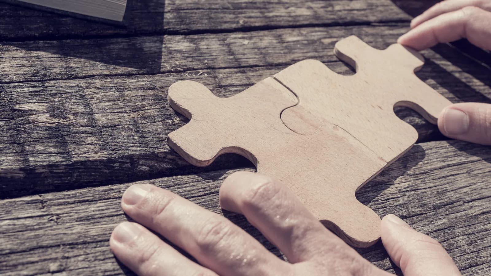 Two hands fitting two large puzzle pieces together on a wooden table